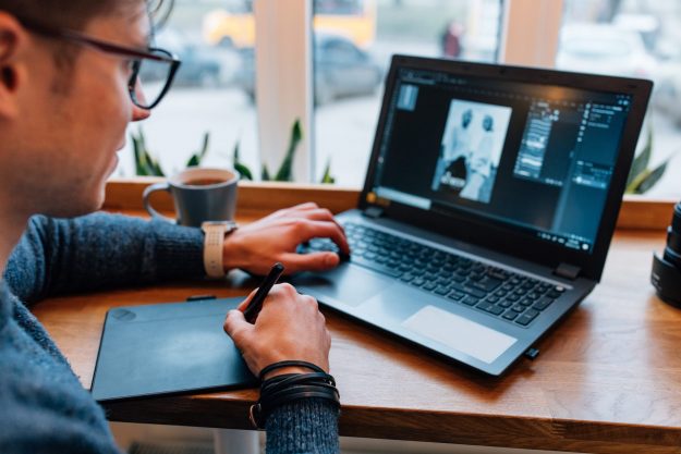 Photographer is processing photo on laptop, sitting at cafe