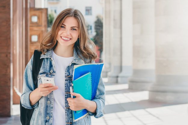 young-girl-student-smiling-against-university-min