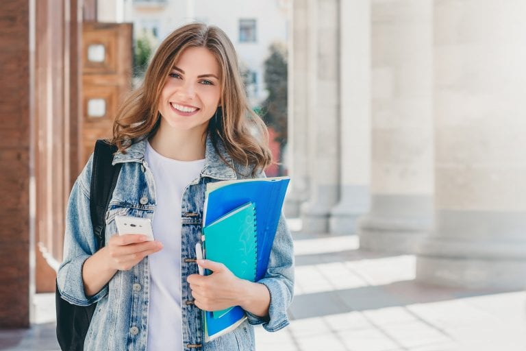 young-girl-student-smiling-against-university-min