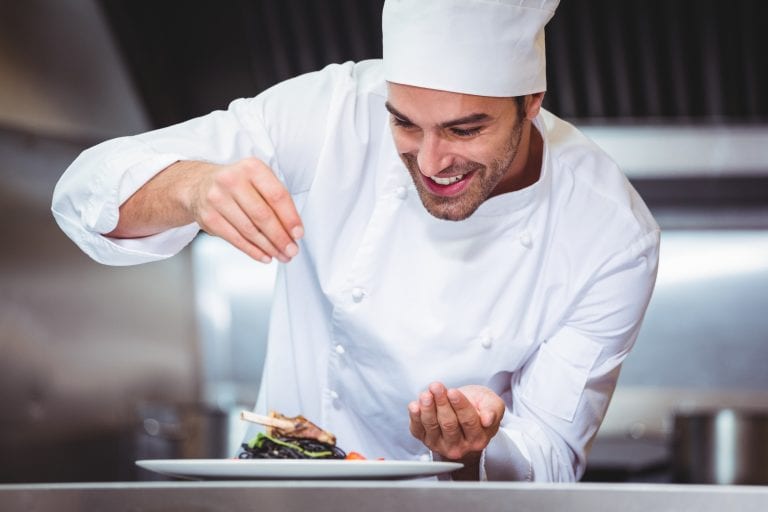 Chef sprinkling spices on dish in commercial kitchen estudiar-cocina-australia