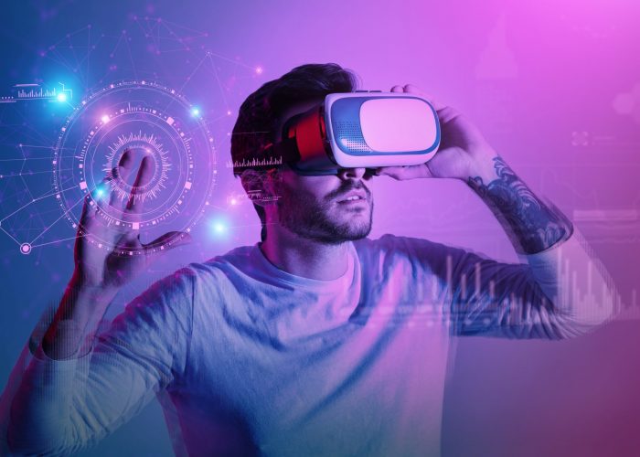 Modern man in VR glasses pressing button at virtual screen with futuristic graphs and charts, colorful background, creative collage