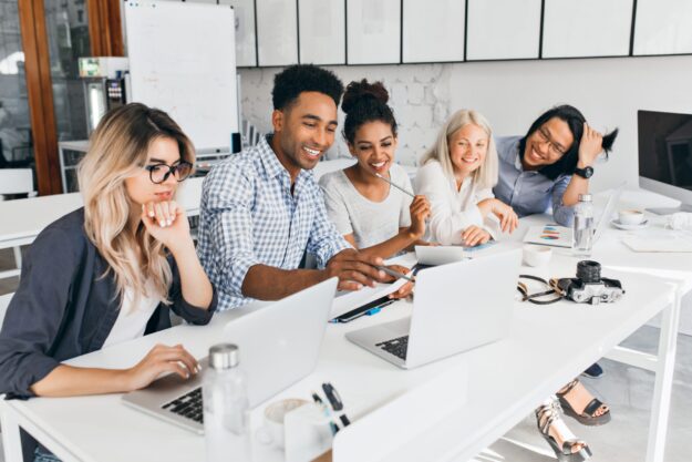 Smiling african student pointing with pencil at laptop screen. Concentrated blonde girl in glasses propping chin with hand while working with computer in office.. Du học Brisbane ngành Kỹ sư phần mềm – Học tập, làm việc và định cư dễ dàng