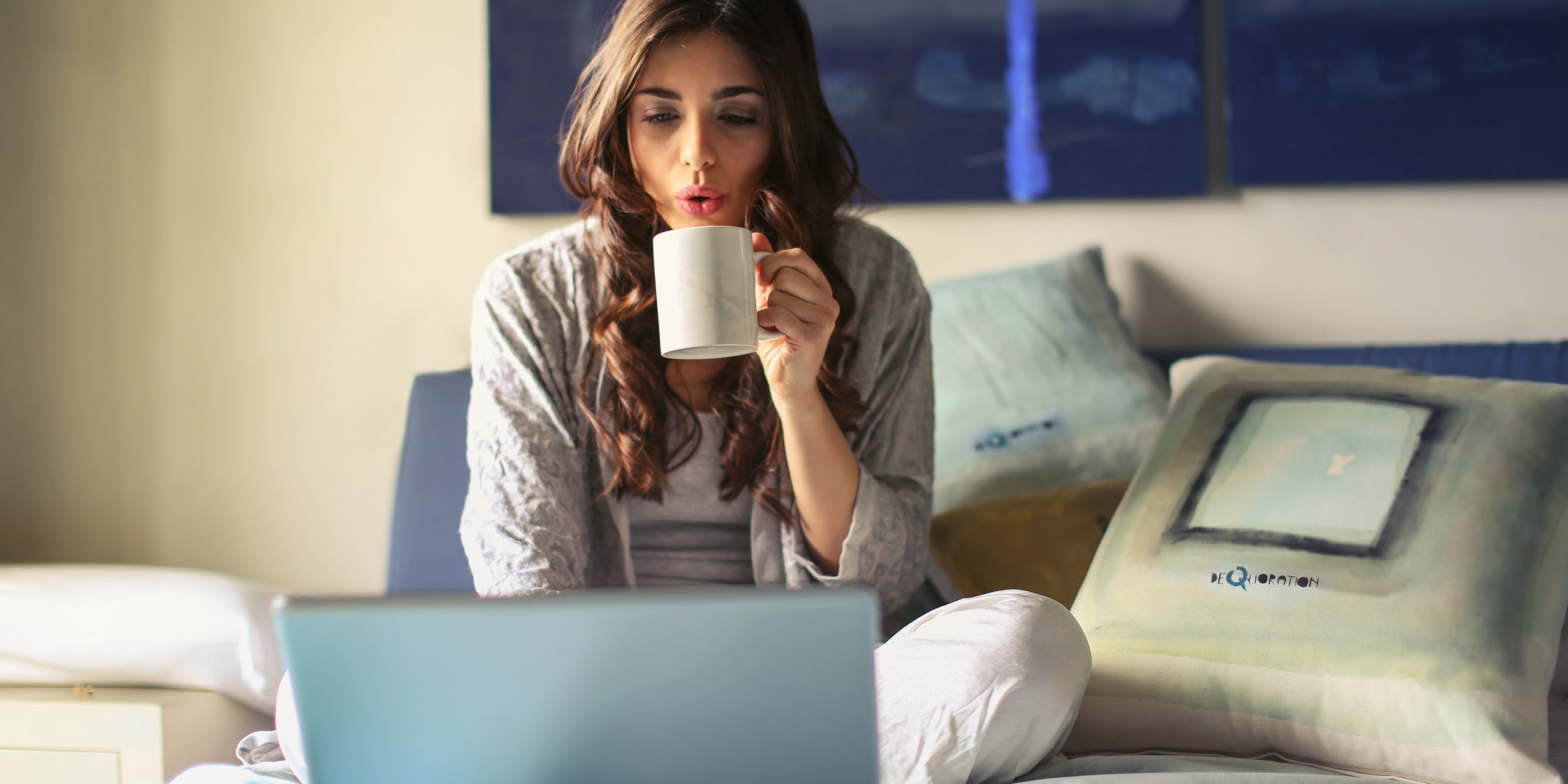 woman-in-grey-jacket-sits-on-bed-uses-grey-laptop-935743